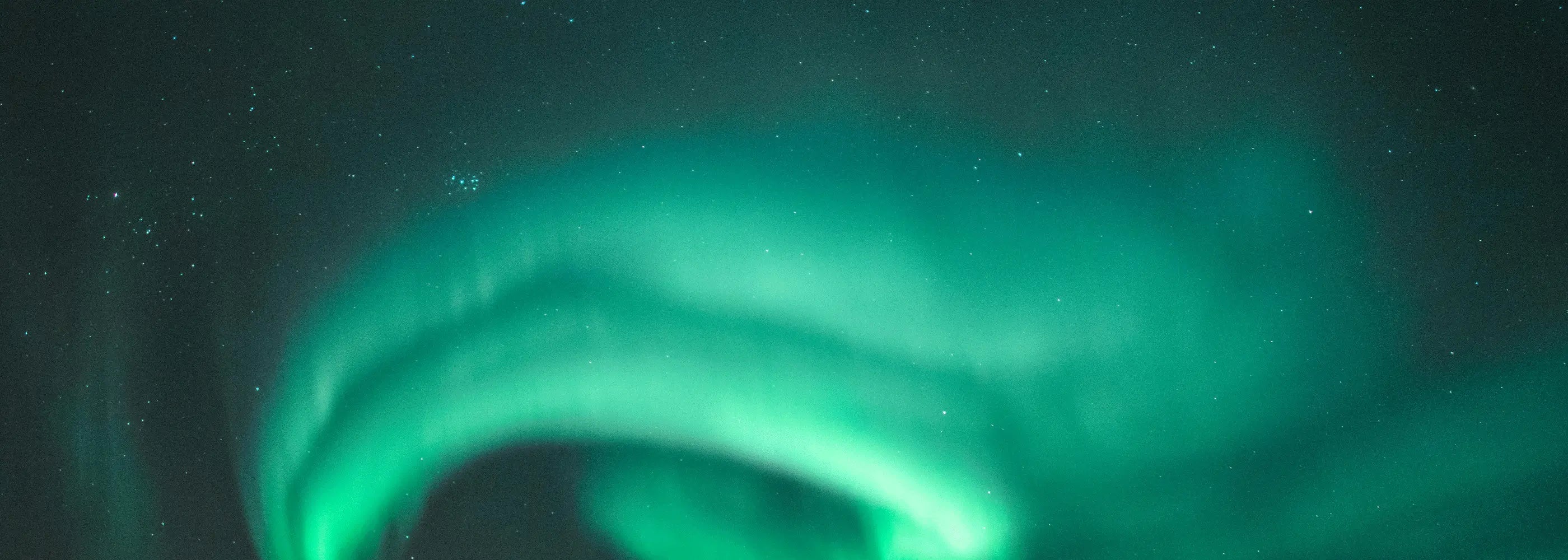 A vibrant green and teal aurora borealis arches across a dark, star-filled night sky.