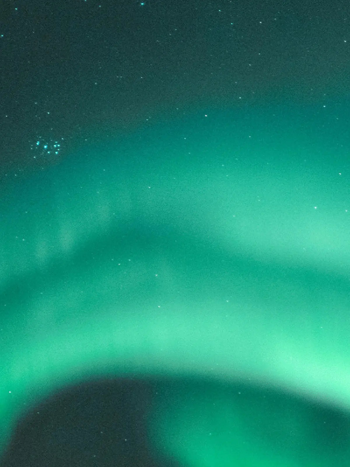 A vibrant green and teal aurora borealis arches across a dark, star-filled night sky.