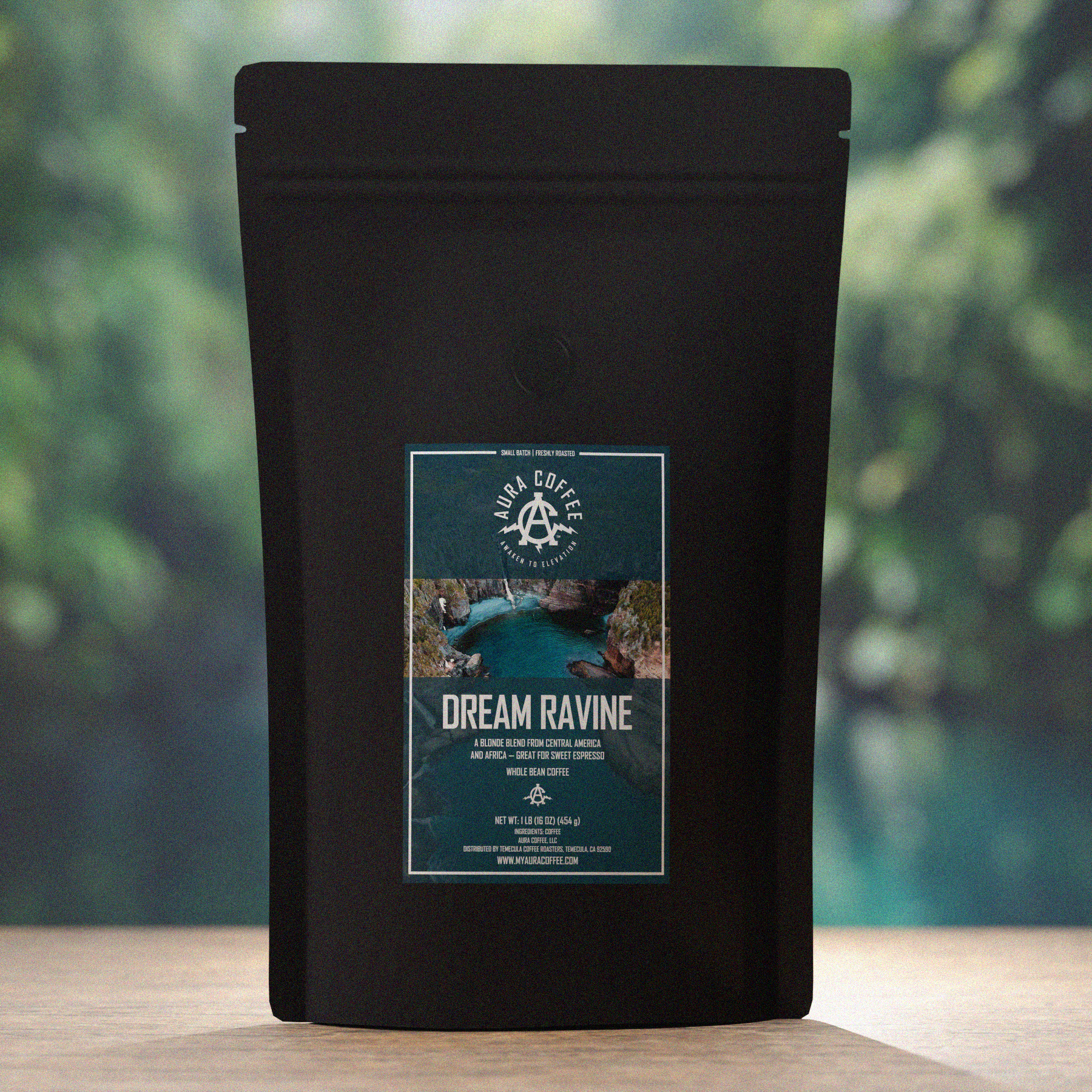 Aura Coffee Dream Ravine Sweet Espresso Blend Pouch on wooden table with trees in the background and a small swimming hole