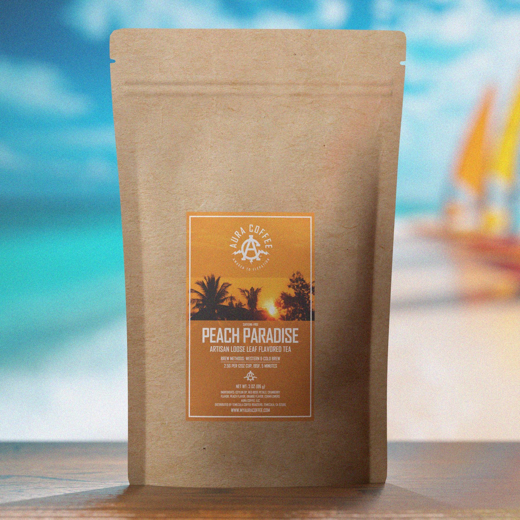 Package of Aura Coffee Peach Paradise Tea on a table on the beach with sailboats in the background