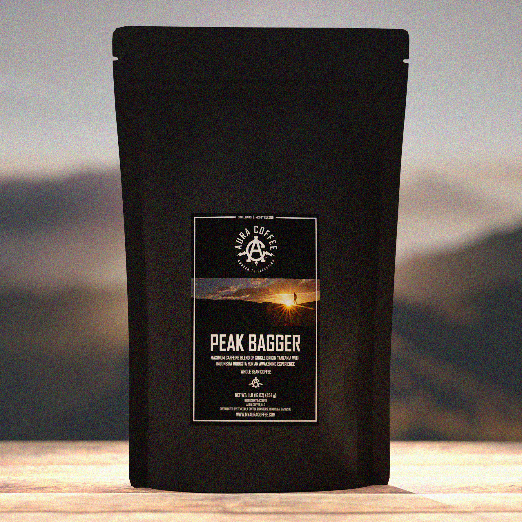 Package of Aura Coffee Peak Bagger Maximum Caffeine Coffee on a table with Mountains in the background